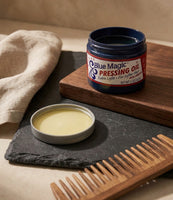 Blue Magic Pressing Oil - open pot op leisteen met houten kam, de gele olie zichtbaar